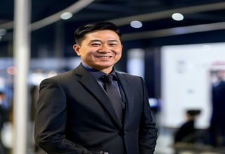 撸撸社官网创始人陈明远身着深色西装，在品牌展板前微笑，神情自信，背景为现代化办公环境